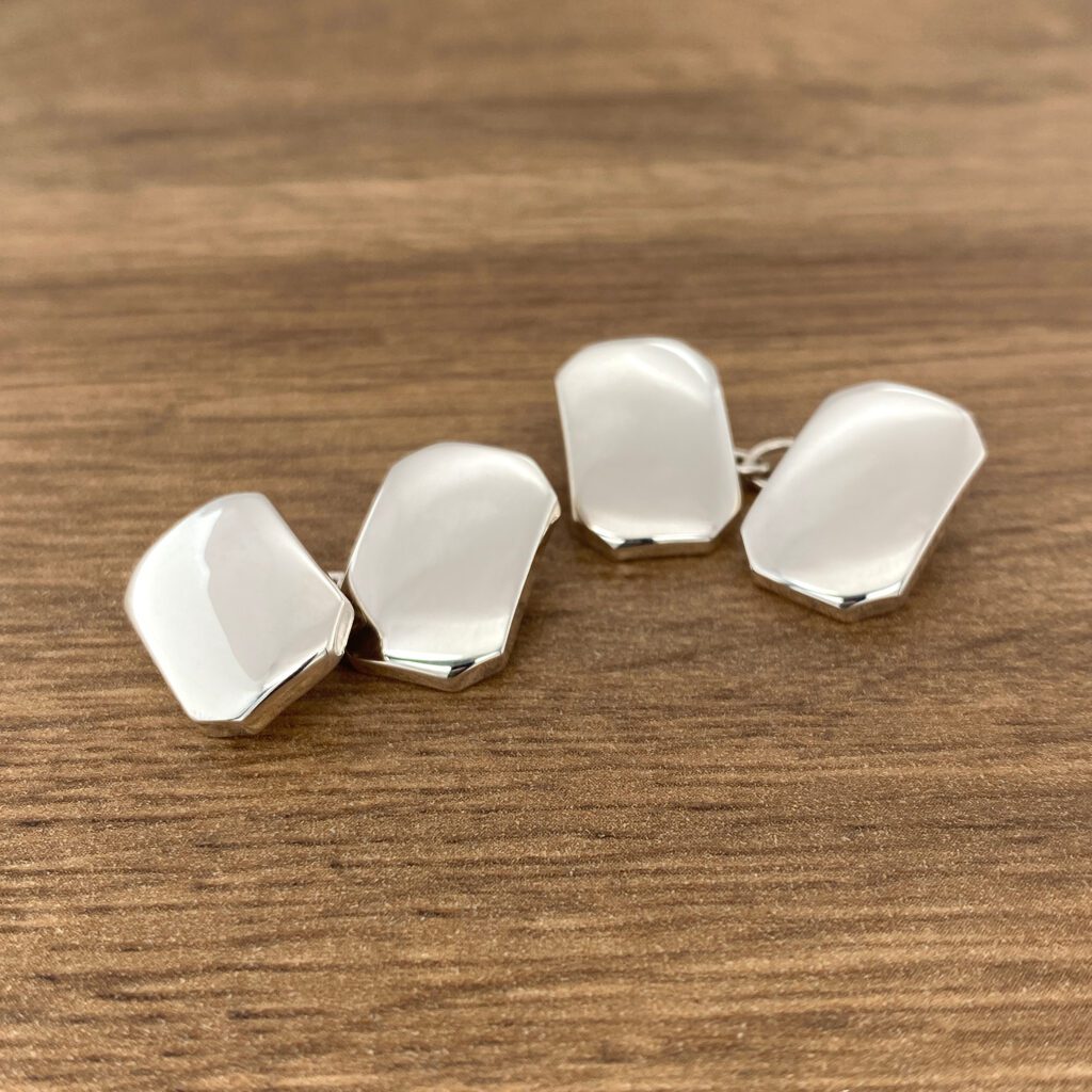 Silver cufflinks on a wooden surface.
