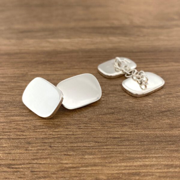 Silver cufflinks on a wooden surface.