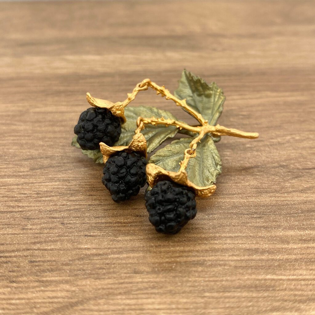 Gold blackberry brooch on wood background.