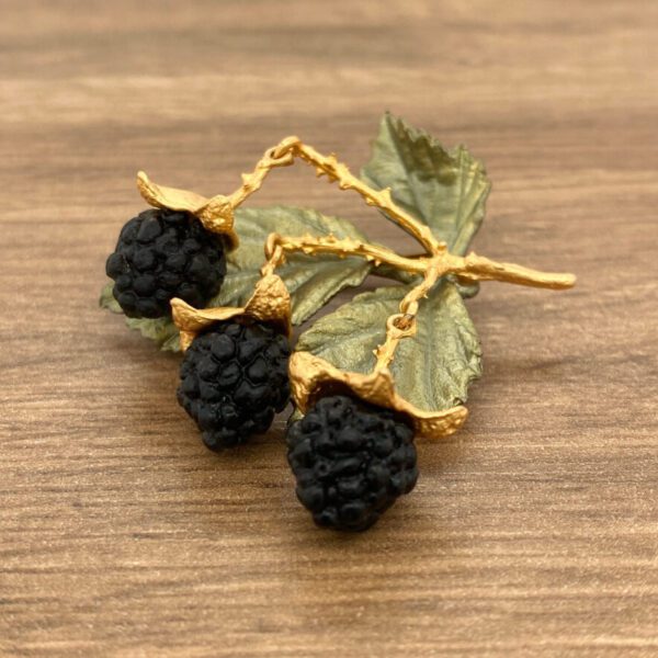 Gold blackberry brooch on wood background.