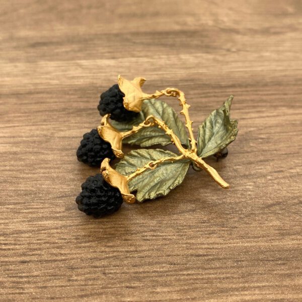 Gold blackberry brooch on wood background.