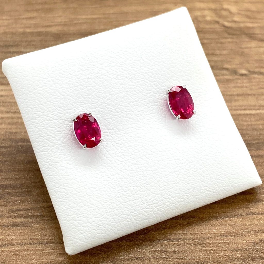 Ruby oval stud earrings on white display.