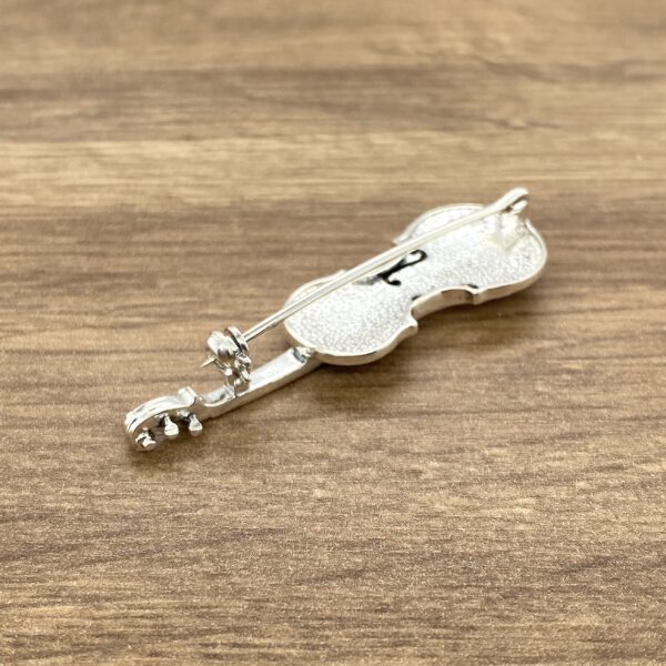 Silver violin pin on wood background.