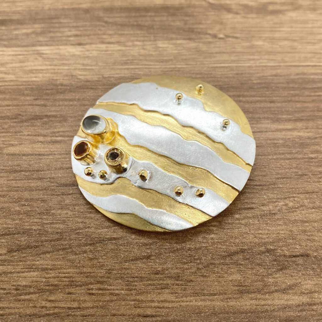 Circular gold and silver gemstone brooch.