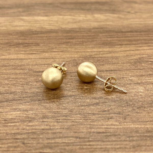 Gold ball stud earrings on wood.