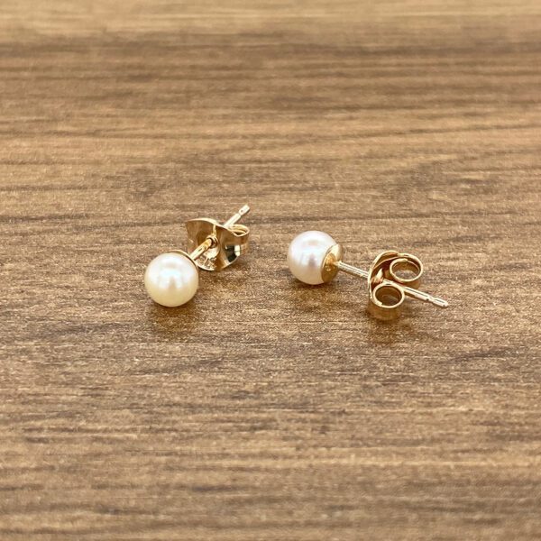 Gold pearl stud earrings on wood.