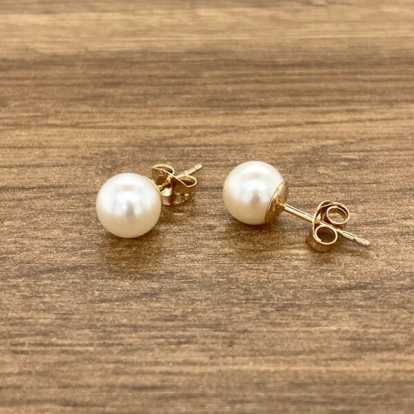 Gold pearl stud earrings on wood.